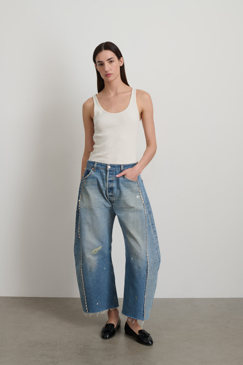 A woman wearing a white tank top and vintage faded indigo blue high-waisted slouchy jeans with hand tatted lace details.